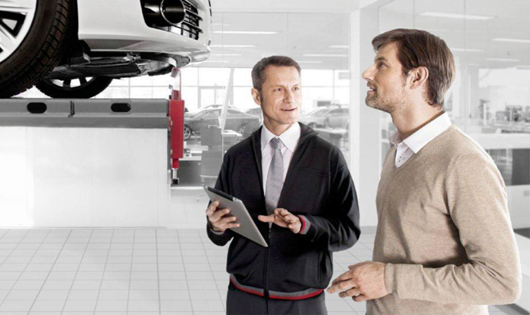 Two males in an Audi service centre looking at a car and iPad